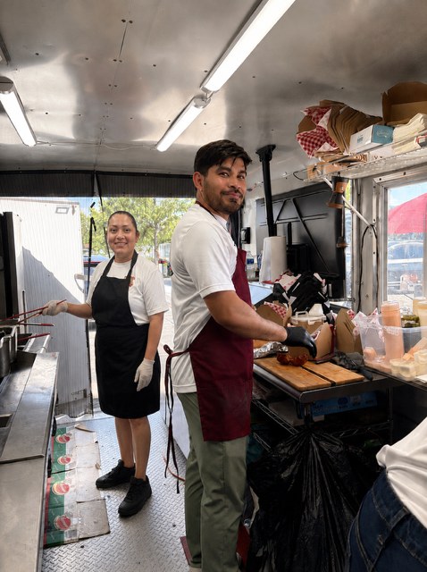 Two CoquiEats cooks smiling while preparing food inside the truck