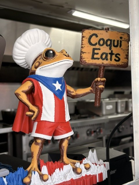 Coquí frog chef figurine holding a CoquiEats sign inside the truck