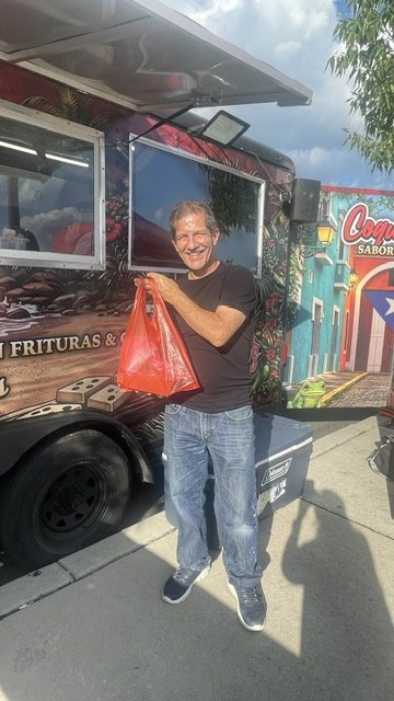 A guest smiling with a bag of CoquiEats takeout beside the truck