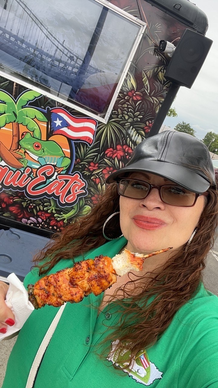 A guest holding a grilled pincho in front of the CoquiEats truck