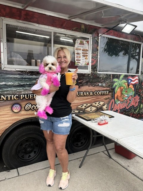 A guest holding a jugo de parcha and a small dog beside the truck