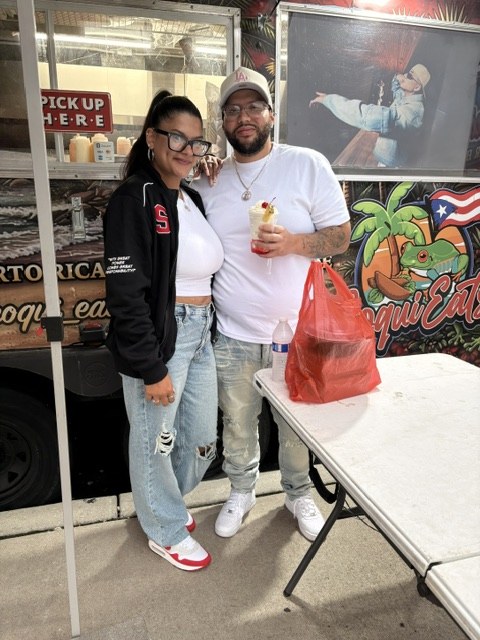 Two guests with drinks and a takeout order beside the CoquiEats truck